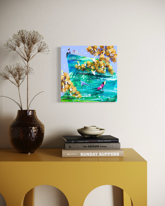 When You’re Ready by Adam Bogusz, square 30 x 30 cm cockatoo painting on MDF board hanging above a mustard yellow console table beside an amber glass vase of dried stems, showing a girl in pink leaning through turquoise water beneath golden gums and a blue sky.