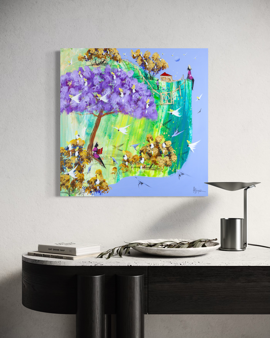 Just a Story by Adam Bogusz, 50 x 50 cm painting on MDF board hanging above a black console with a travertine top, a stone bowl holding an olive branch, books and a metal lamp, showing a purple jacaranda full of cockatoos and a girl reading beneath it.