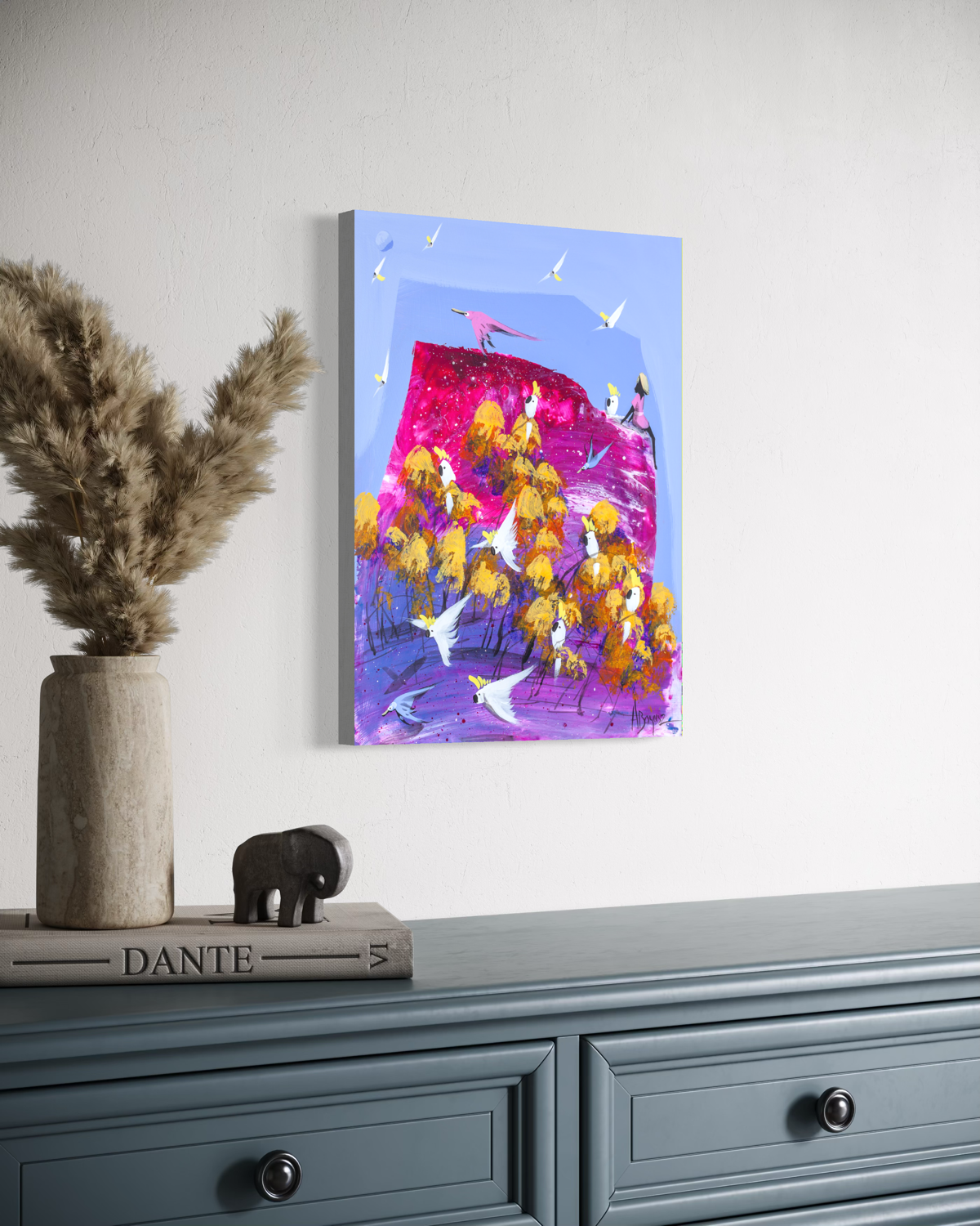 Good Company by Adam Bogusz hanging unframed on a pale wall above a blue grey sideboard with dried pampas and a carved elephant, seen at a slight angle so the depth of the painted board is visible.