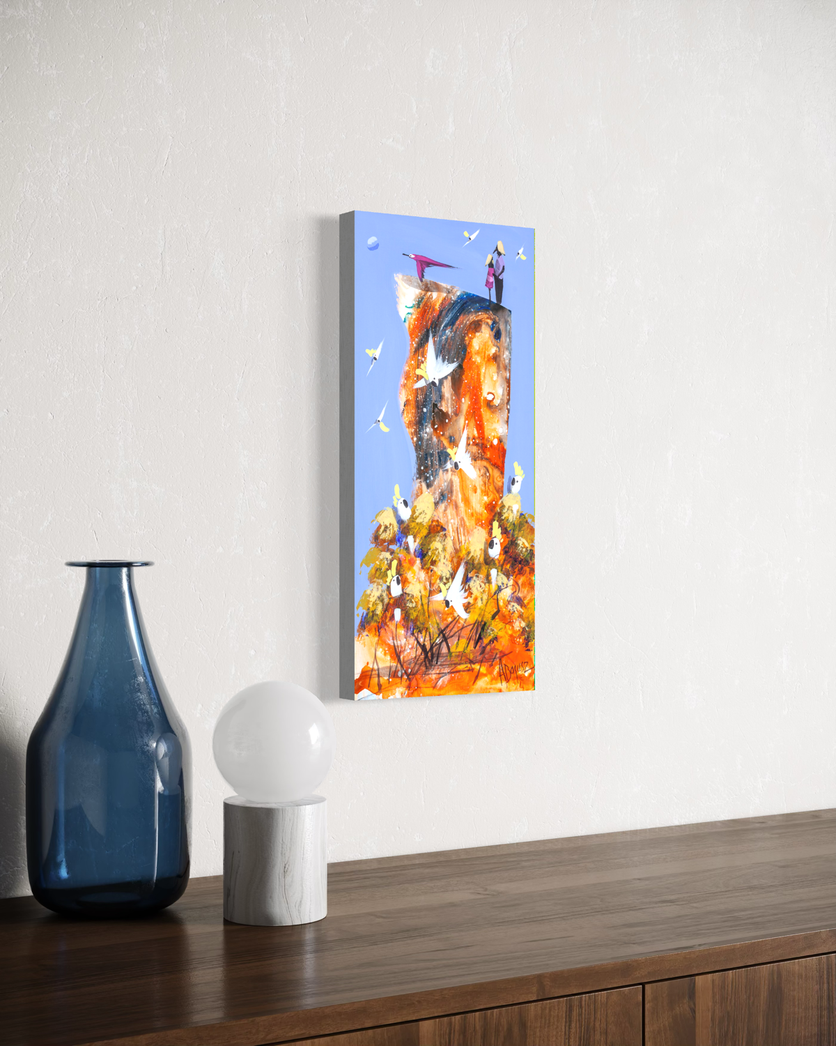 Side by Side by Adam Bogusz hanging unframed on a pale textured wall above a dark timber sideboard with a blue glass bottle and globe lamp, seen at a slight angle so the depth of the painted board is visible.